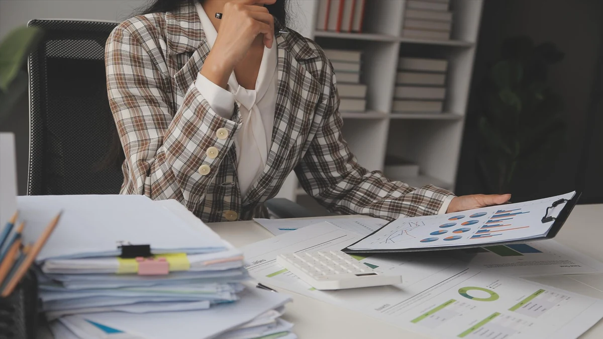 Business owner at a desk surrounded by spreadsheet printouts and a laptop